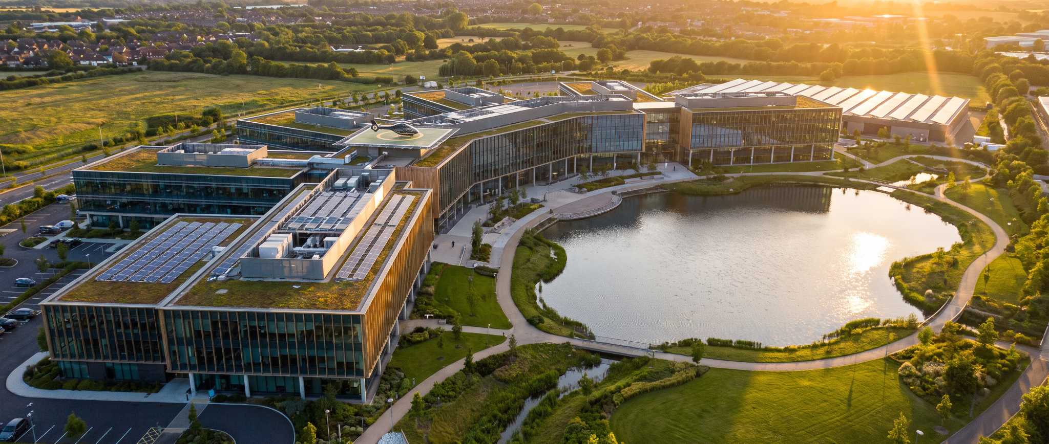 Illustrative aerial view of a corporate campus beside a lake at golden hour